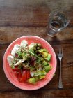 Teller mit Salat und Glas Wasser auf Holztisch — Stockfoto