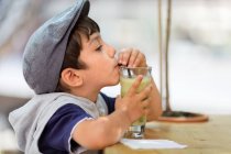 Маленький хлопчик у кепці п'є сік — стокове фото