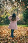 Visão traseira de uma menina de pé em folhas de outono — Fotografia de Stock
