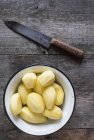 Batatas descascadas na tigela e faca na mesa de madeira — Fotografia de Stock