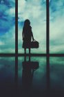 Silhouette di una ragazza in piedi alla finestra di un aeroporto — Foto stock