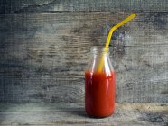 Tomato juice in glass bottle with straw — Stock Photo