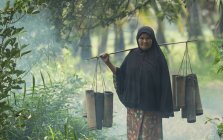 Senior Thai woman carrying bamboo tubes with sugar, Thailand — Stock Photo