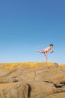 Menino de pé em uma perna em uma rocha na frente do céu azul — Fotografia de Stock