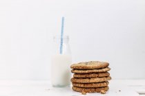 Montón de galletas y botella de leche con una paja sobre fondo blanco - foto de stock