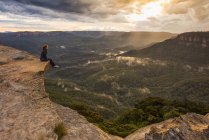 Mujer sentada en la cornisa de las montañas, Parque Nacional Blue Mountains, Nueva Gales del Sur, Australia - foto de stock