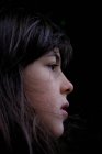 Profil des nachdenklichen Mädchens mit dunklen Haaren auf schwarzem Hintergrund — Stockfoto