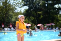 Chica de pie cerca de la piscina con un chaleco salvavidas - foto de stock