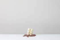 Концептуальний бар з білого шоколаду в басейні розтопленого молочного шоколаду — стокове фото