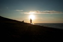 Силуэт человека, бегущего по пляжу на закате — стоковое фото