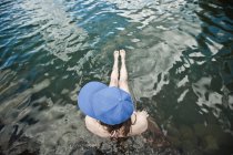 Mujer con gorra sentada en el borde de un lago - foto de stock