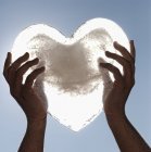 Imagen recortada de la persona que sostiene el corazón congelado contra el cielo - foto de stock