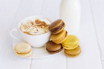 Macaroons, milk and cup of coffee over wooden background — Stock Photo