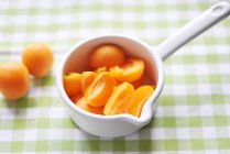 Bowl of fresh sliced apricots on checkered tablecloth — Stock Photo