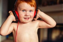 Усміхнений імбирний хлопчик слухає музику з навушниками — стокове фото