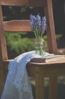 Grape hyacinth flowers in jar with book and napkin on wooden chair outdoors — Stock Photo