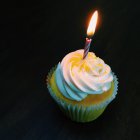 Cupcake avec une bougie solitaire sur fond noir — Photo de stock