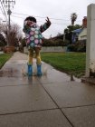 Девушка в узорчатом дождевике прыгает в лужу — стоковое фото