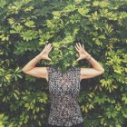 Donna con volto nascosto dietro le foglie in piedi con le braccia alzate — Foto stock