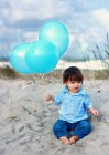 Baby boy sitting on sand with blue balloons — Stock Photo