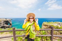 Mujer sosteniendo sombrero en un cabo Manzamo, Okinawa, Japón - foto de stock