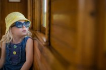 Девушка в летней шляпе и солнцезащитных очках сидит в поезде и смотрит в окно — стоковое фото
