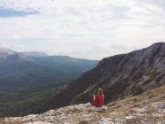 Vista trasera de una mujer sentada en la montaña y mirando a la vista - foto de stock