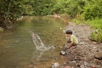 Хлопчик грає і бризкає воду на березі річки — стокове фото
