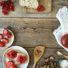 Fresas, grosellas rojas, pan y mermelada sobre mesa rústica de madera - foto de stock