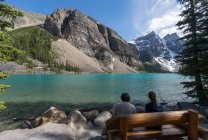 Dos personas sentadas junto al lago Moraine, Parque Nacional Banff, Rockies Canadienses, Alberta, Canadá - foto de stock
