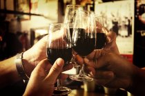Quatro pessoas brindam com copos de vinho tinto, close-up — Fotografia de Stock