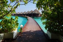 Scenic view of along elevated footbridge leading across water to row of stilt huts, Maldives — Stock Photo