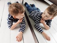 Portrait of a beautiful little Boy lying on the floor looking at himself in the mirror — Stock Photo