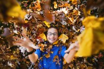 Niño acostado en la espalda y jugando con hojas de otoño - foto de stock