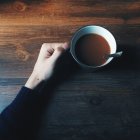 Cropped image of Hand holding mug of hot chocolate on wooden table, top view — Stock Photo