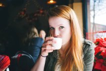 Портрет молодой женщины, потягивающей из белой чашки в ресторане — стоковое фото
