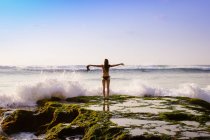 Indonesia, Bali, Woman standing in front of sea with arms raised — Stock Photo