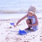 Девушка в соломенной шляпе играет на пляже с пластиковой лопатой — стоковое фото
