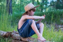 Молодий хлопчик у солом'яному капелюсі сидить на колоді — стокове фото