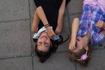 Visão de alto ângulo de duas irmãs bonitos deitado no chão e rindo — Fotografia de Stock