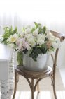 Eimer mit schönen zarten Blumen auf Stuhl drinnen — Stockfoto