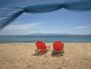 Greece, Thassos, Red lounge chairs on beach — Stock Photo