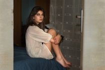 Junge Frau sitzt zu Hause im Bett und blickt in die Kamera — Stockfoto