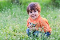 Улыбающийся мальчик, сидящий в траве — стоковое фото