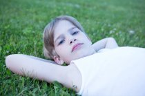 Portrait de garçon blond étendu sur l'herbe avec les mains derrière la tête — Photo de stock