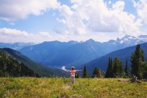 Petit garçon debout avec les bras tendus dans la nature et regardant les montagnes — Photo de stock