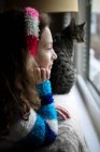Side view of beautiful girl with cute tabby cat looking out of window — Stock Photo