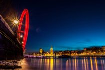 London Eye in motion and illuminated cityscape reflecting in river, London, UK — Stock Photo