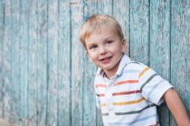 Porträt eines lächelnden Jungen, der vor einer schäbigen Holzwand steht — Stockfoto