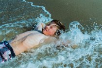 Menino deitado no surf na praia arenosa — Fotografia de Stock